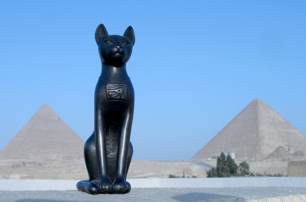 This image has an empty alt attribute; its file name is Bastet-in-front-of-pyramidsweb-1024x677.jpg